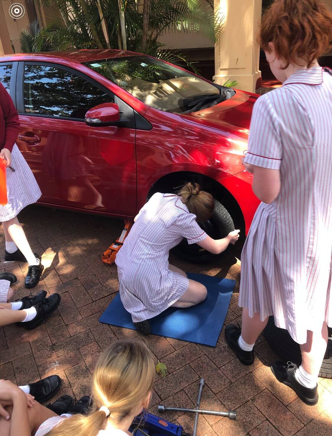 Girls learning how to change tires at Stella Maris College