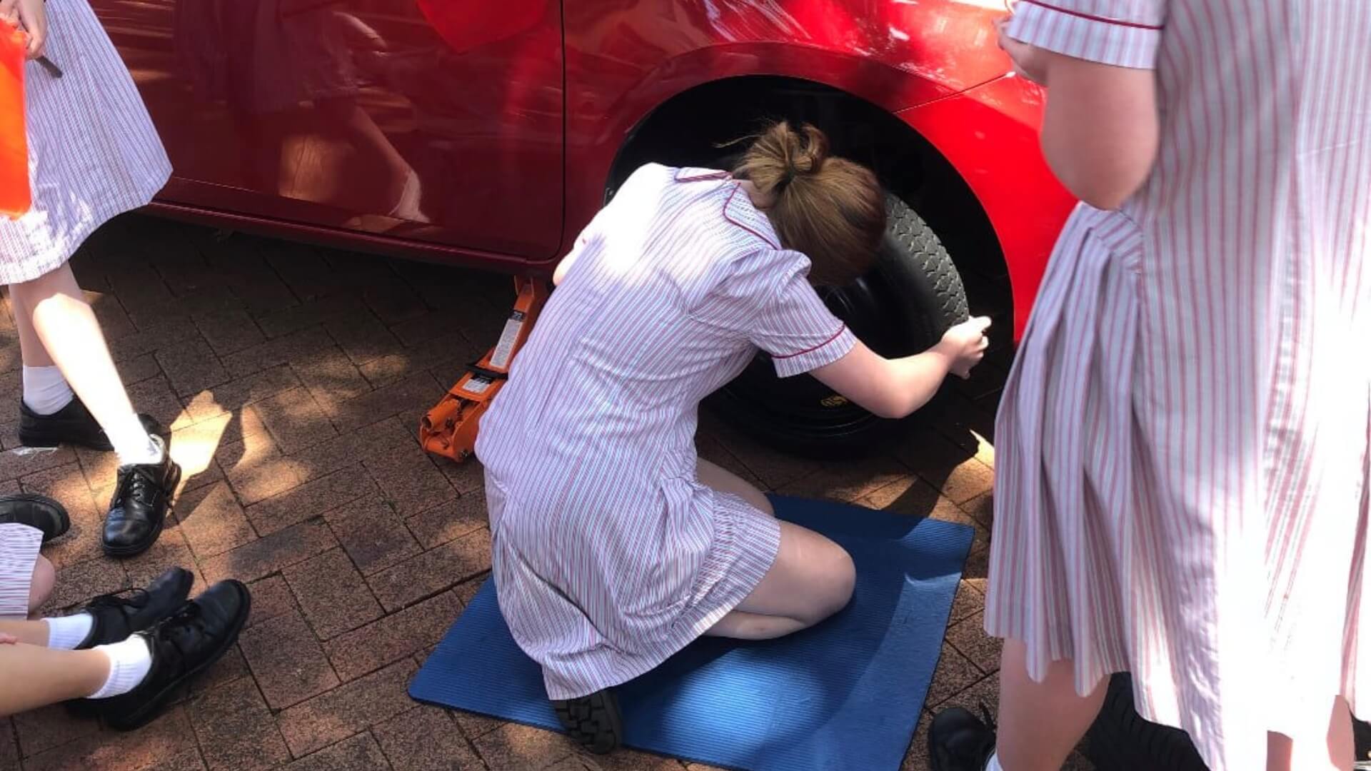Girls learning how to change tires at Stella Maris College